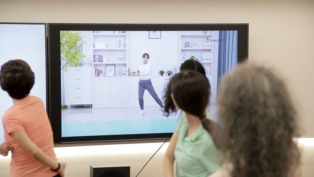 대형 화면으로 메모핏 운동 영상을 보는 운동교실 참여자들